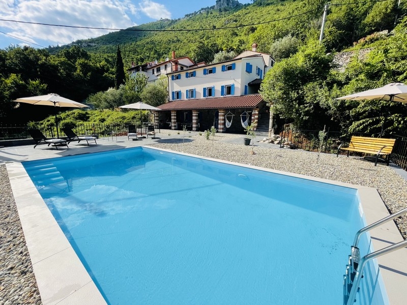 A villa külső kilátása kék medencével, napozóterasszal és a környező természettel