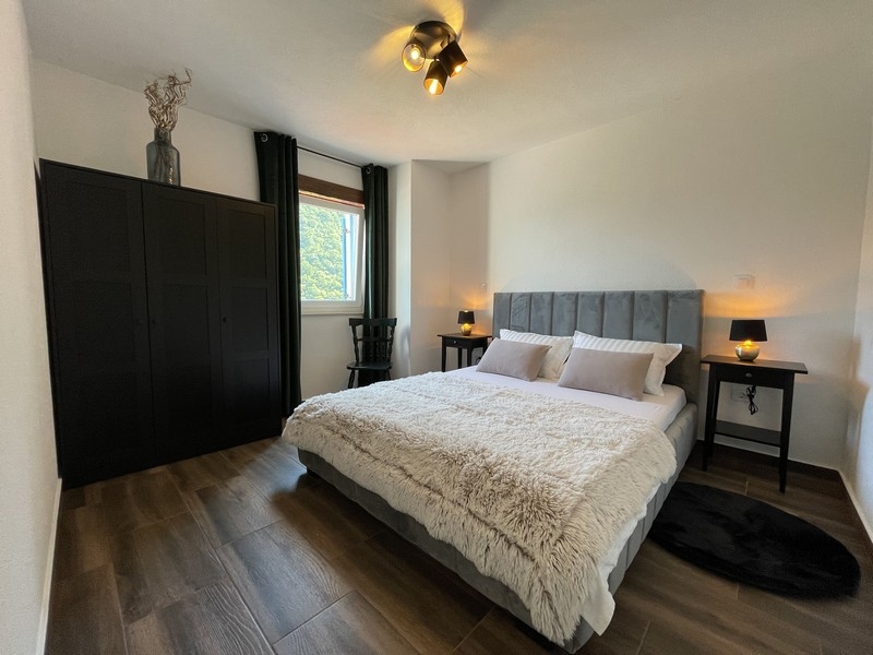 Hálószoba szürke ággyal, fekete gardróbbal és két meleg fénnyel megvilágított éjjeliszekrénnyel