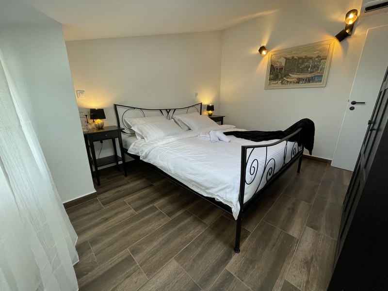 Hálószoba kovácsoltvas ággyal, fa padló- és fali lámpákkal, oldalnézetből egy festményre