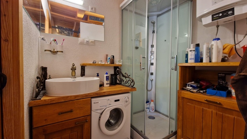 Fürdőszoba zuhanykabinnal, mosógéppel és fapolcokkal.