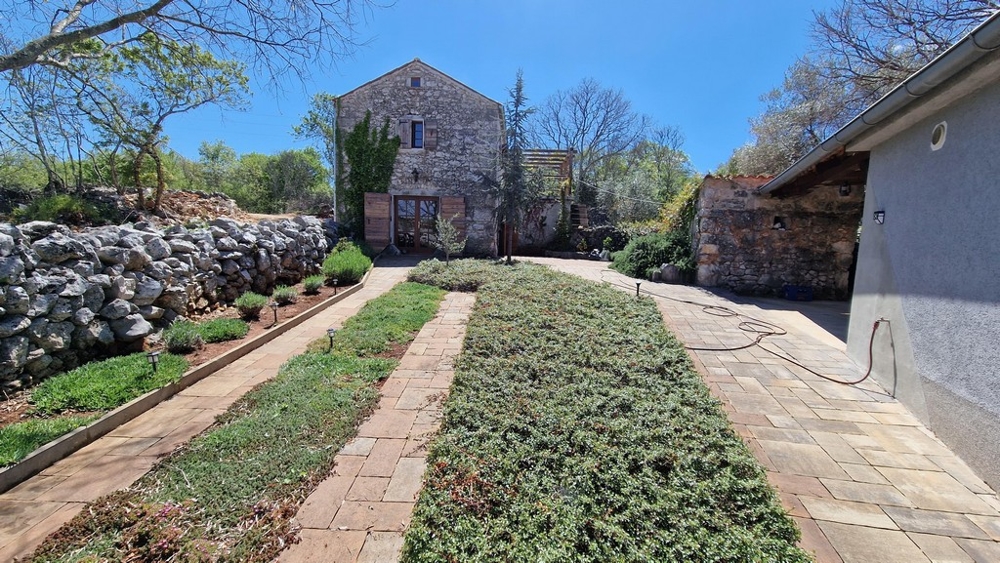 Gondozott kert, aszfaltozott ösvény, háttérben kőház.