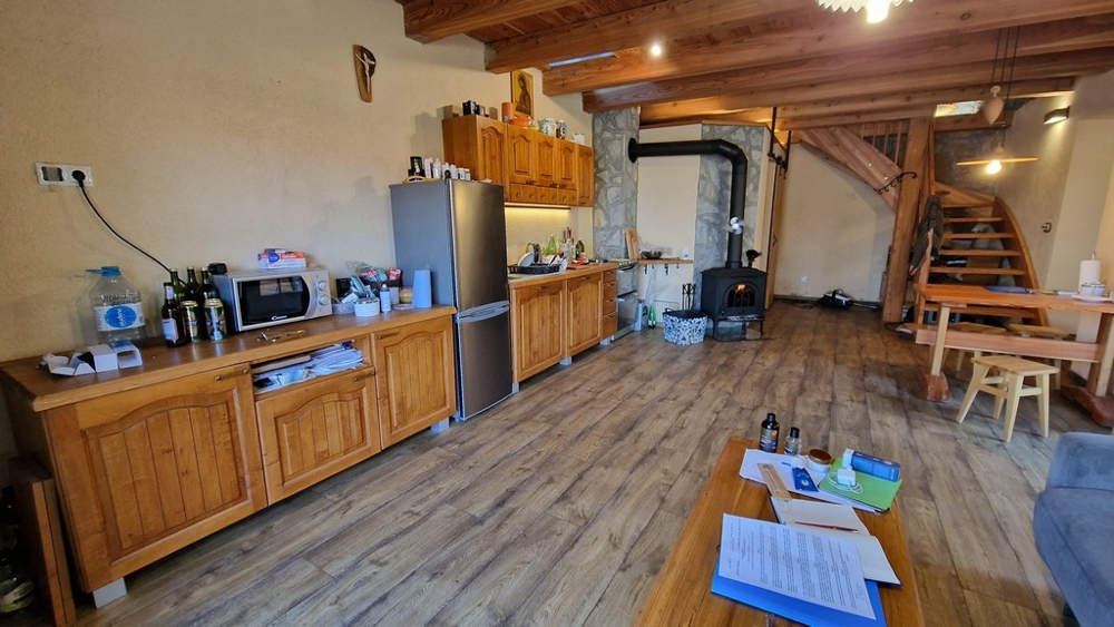 Konyha fa szekrényekkel, hűtőszekrénnyel és rusztikus stílusú étkezőasztallal.