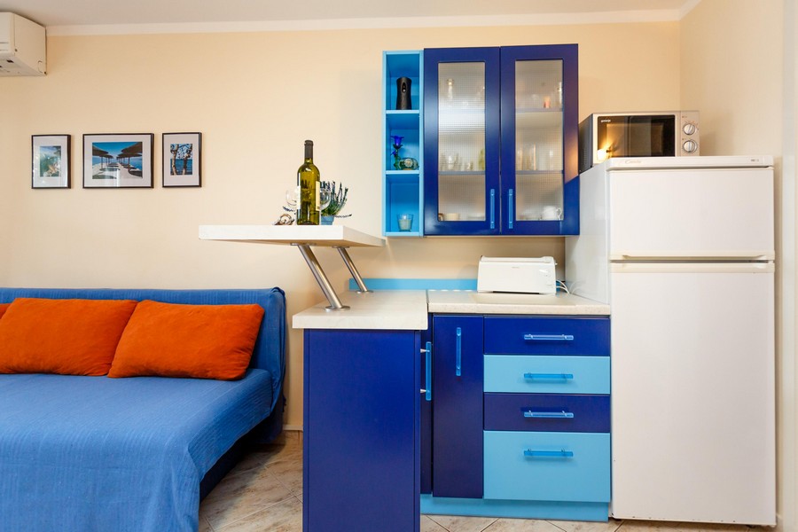 Konyha kék szekrényekkel, fehér hűtőszekrénnyel és kis konyhai eszközökkel