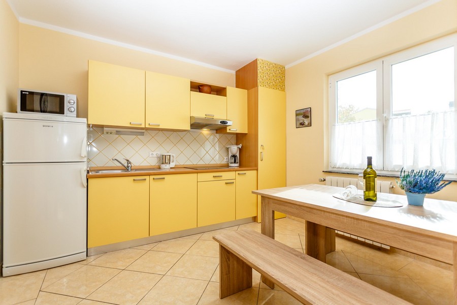 Sárga konyha étkezőasztallal és padokkal, a falakon világos csempe