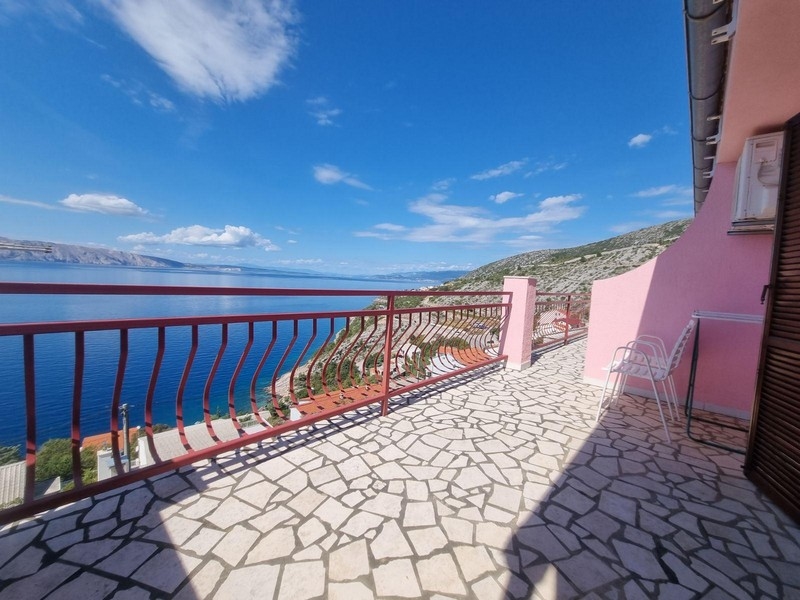 Nagy nyitott terasz mozaik kőpadlóval, piros korlátokkal és kilátással a tengerre és a környező vidékre.