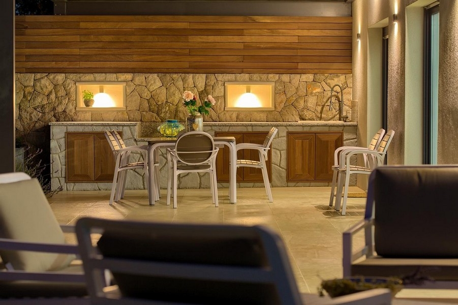 Fedett szabadtéri étkező kőből készült konyhasarokkal és fa szekrényekkel, stílusosan megvilágítva