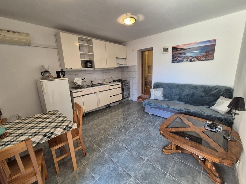 Nyitott nappali konyhával, étkezőasztallal és kanapéval, járólapozott padlóval.