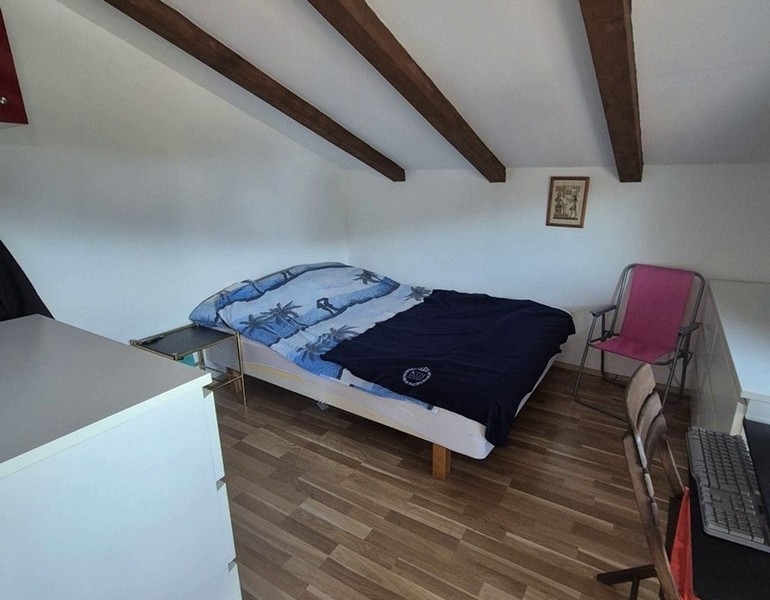 Hálószoba a tetőtérben fagerendákkal és franciaággyal.