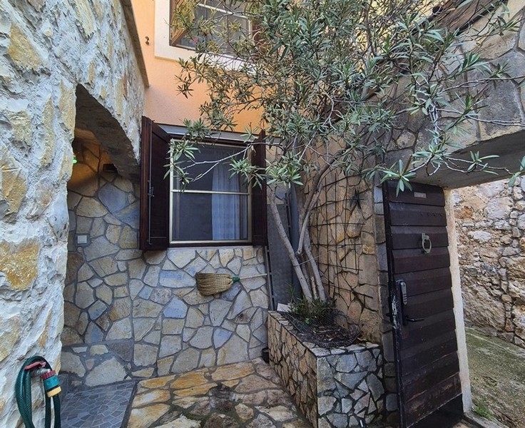 Kis udvar kőfallal és olajfával, valamint bejárati ajtóval.