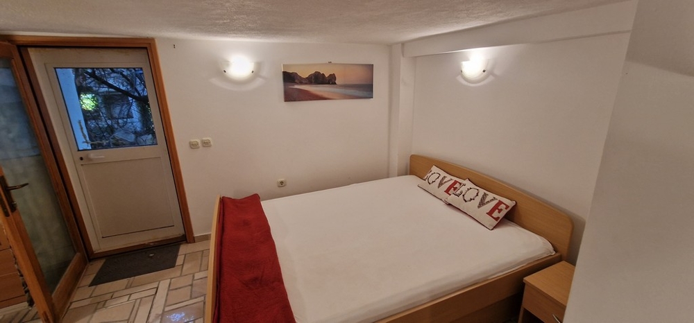 Egy hálószoba franciaággyal, fehér és piros díszítéssel. A falon egy strand képe, és egy ajtó kifelé vezet.