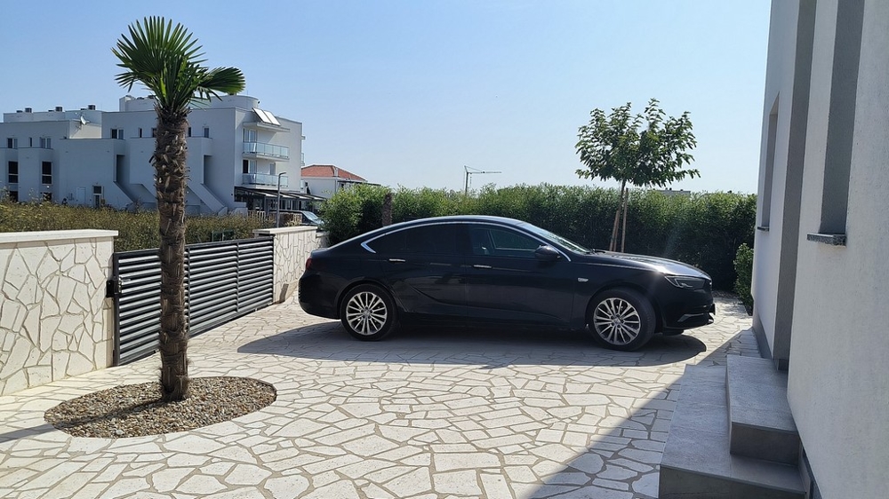 Bejárat autóval, pálmafákkal és kőfallal.