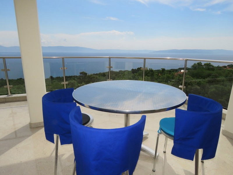 Erkély gyönyörű kilátással a tengerre és étkezősarok kék székekkel.