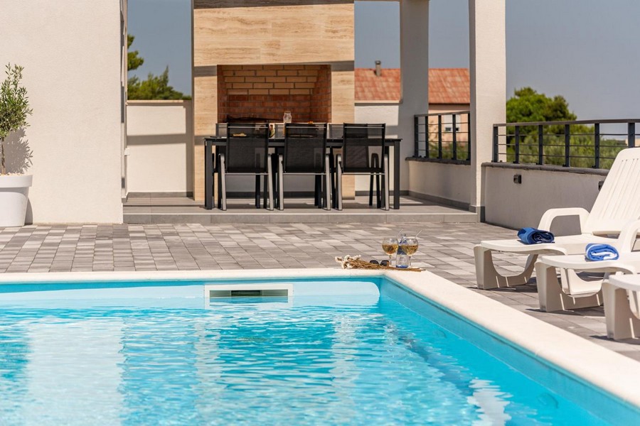 Külső rész úszómedencével, napozóágyakkal és grillezővel a háttérben.