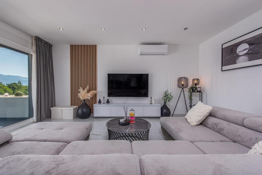 Modern nappali szürke kanapéval, televízióval és fából készült díszítőfallal, világos márványpadlóval és dekorációval.