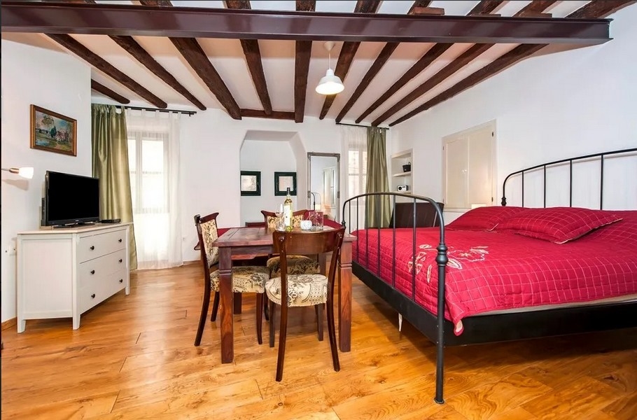 Világos apartman ággyal, fagerendákkal és asztallal