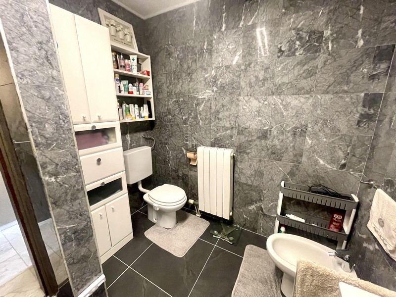 Fürdőszoba WC-vel, bidével és szürke fali csempével