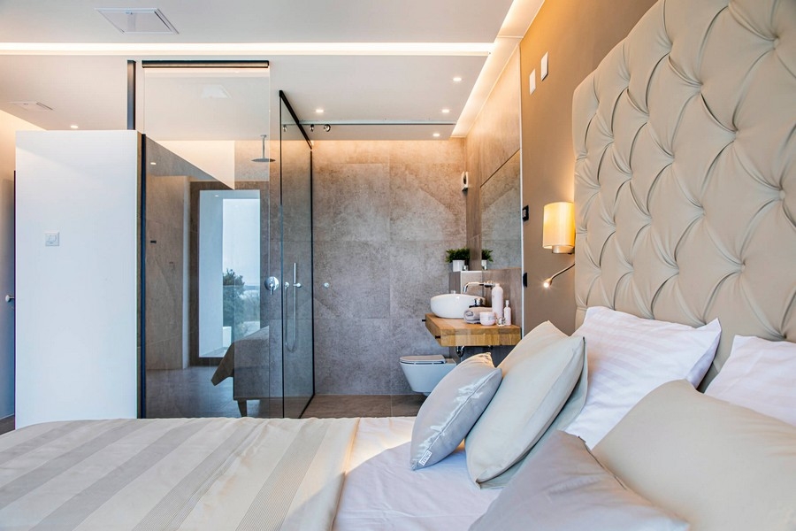 Hálószoba üveg fürdőszobával és bézs fejtámlával.