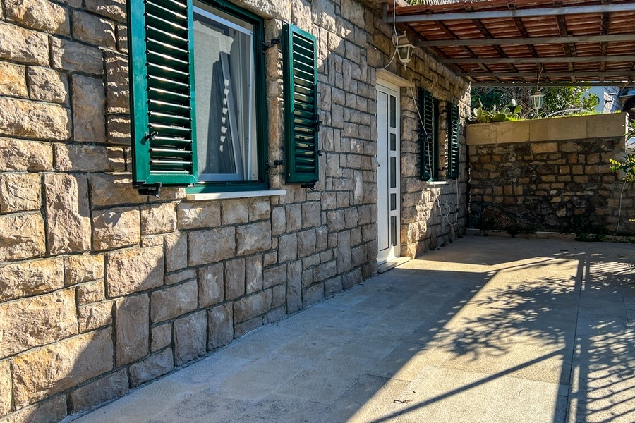 Kő terasz, ahonnan be lehet jutni a házba, zöld redőnnyel